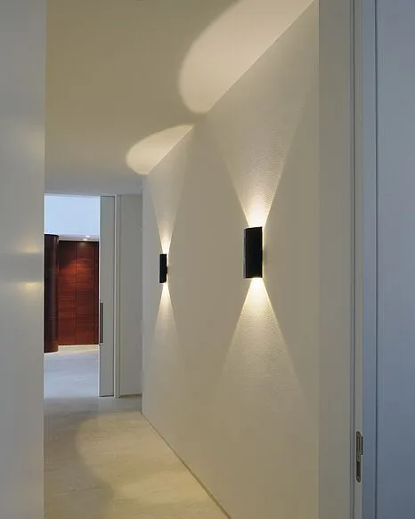 Aplique Espiral: apliques negros en un pasillo blanco, con haces de luz hacia arriba y hacia abajo